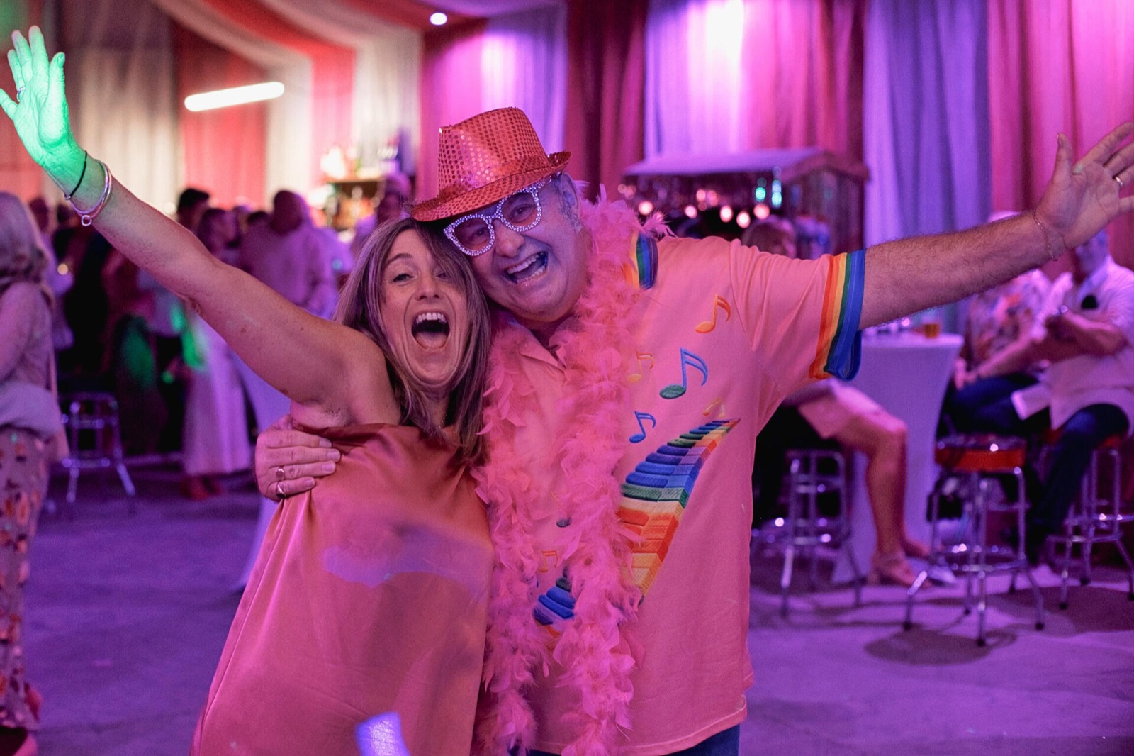 Two guests laughing with arms outstretched at a party